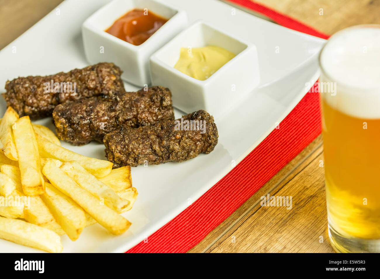 Tradizionale rumena Mici e patate fritte con ketchup, senape e bicchiere di birra Foto Stock
