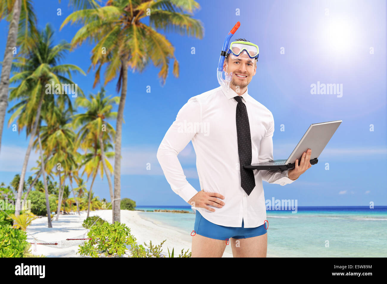 Imprenditore con una maschera subacquea in possesso di un computer portatile e in piedi su una spiaggia Foto Stock