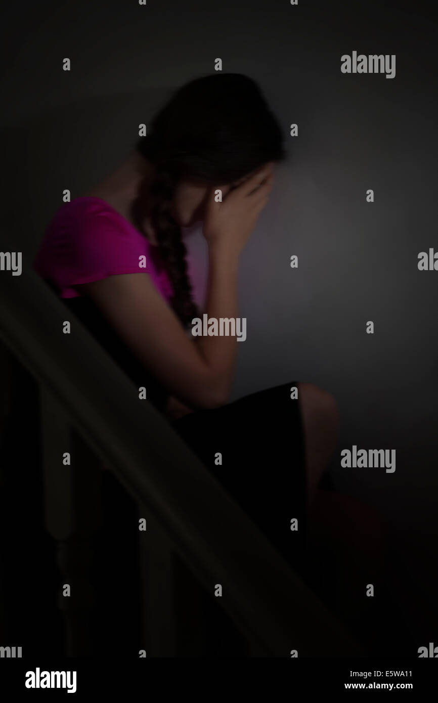 Moody colpo di una giovane donna seduta da sola al buio con la mano che copre il volto. La depressione e l'umore. Foto Stock