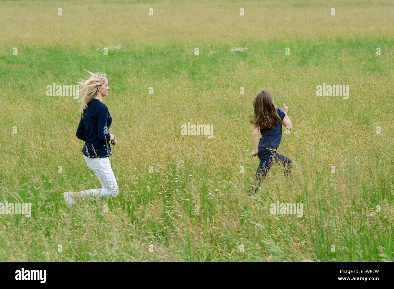 Madre e figlia in esecuzione attraverso il lungo campo di erba Foto Stock