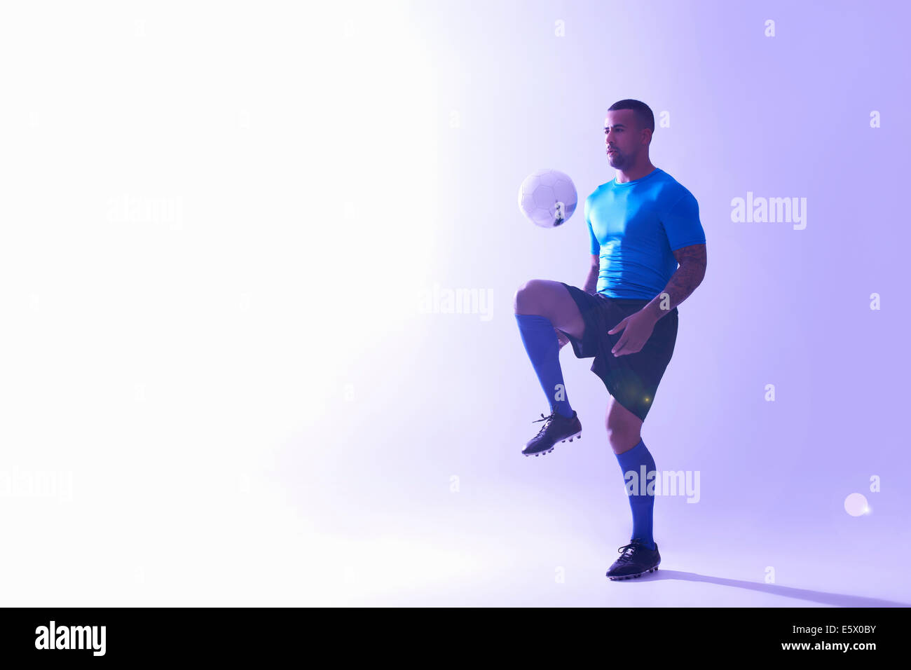 Studio shot del maschio giovane giocatore di calcio mantenendo la sfera metà aria con il ginocchio Foto Stock