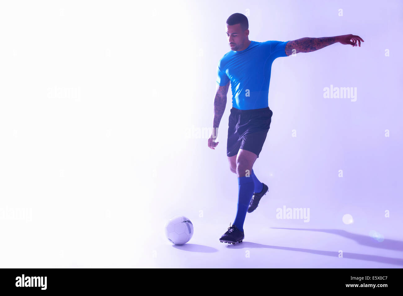 Studio shot del maschio giovane giocatore di calcio calciare la palla Foto Stock