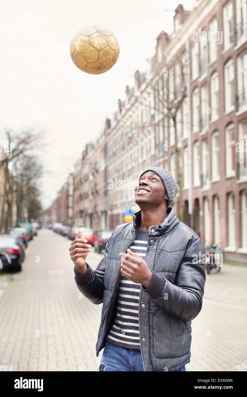 Giovane uomo sulla strada gettando pallone da calcio, Amsterdam, Paesi Bassi Foto Stock