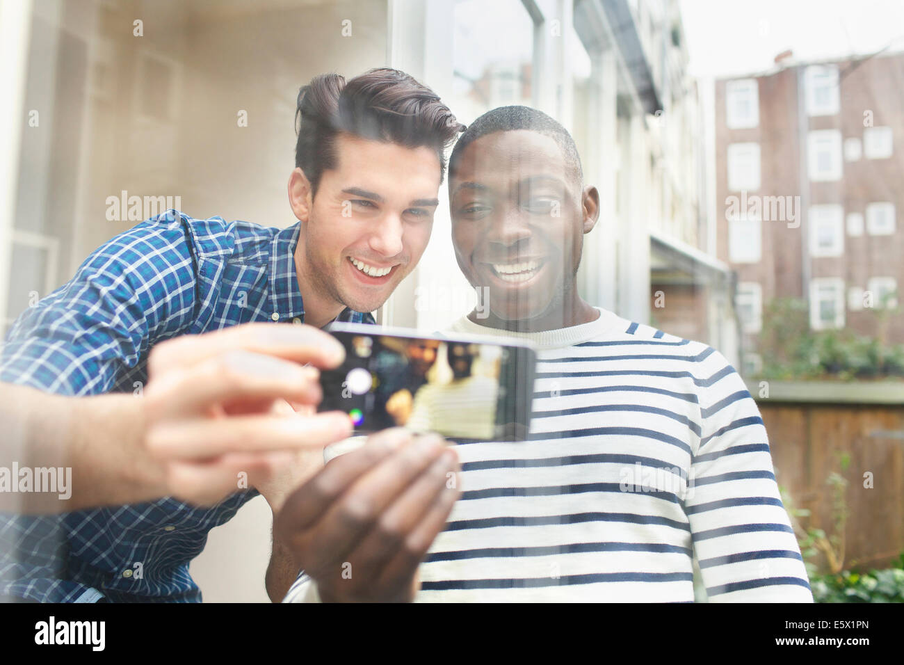 Due giovani amici maschi tenendo selfie patio dietro il vetro Foto Stock