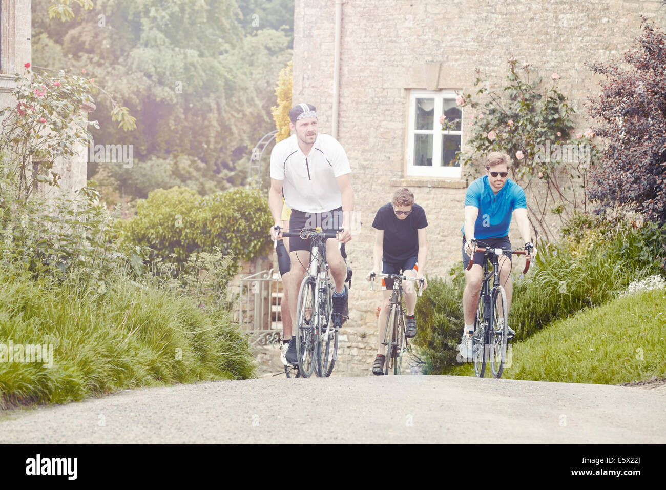 I ciclisti in sella attraverso il villaggio, Cotswolds, REGNO UNITO Foto Stock