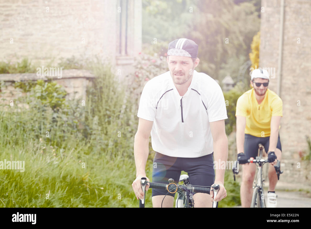 I ciclisti in sella attraverso il villaggio, Cotswolds, REGNO UNITO Foto Stock