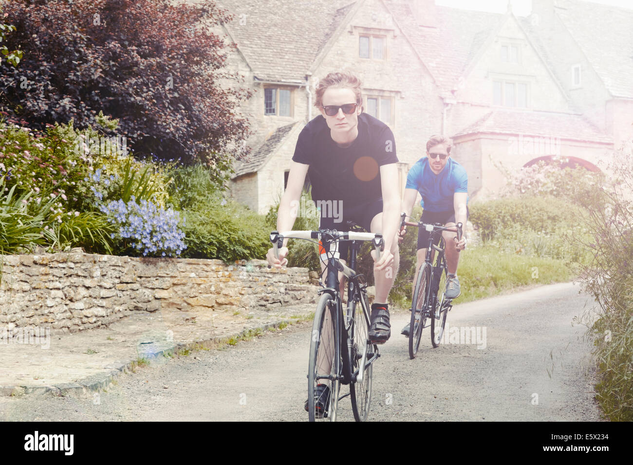 I ciclisti in sella attraverso il villaggio, Cotswolds, REGNO UNITO Foto Stock
