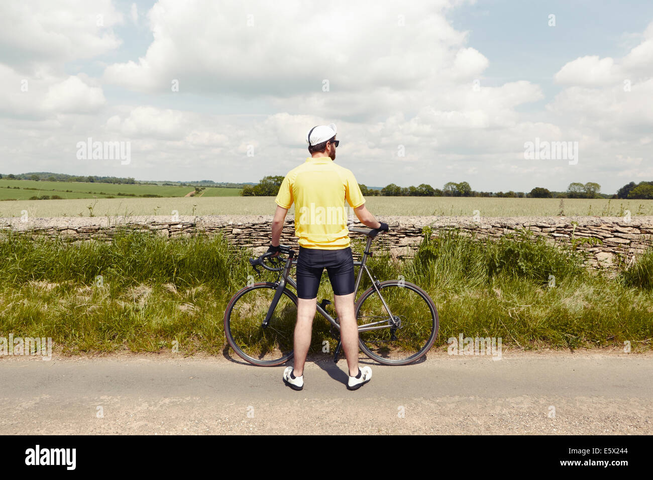 Ciclista in piedi da muro di pietra, Cotswolds, REGNO UNITO Foto Stock