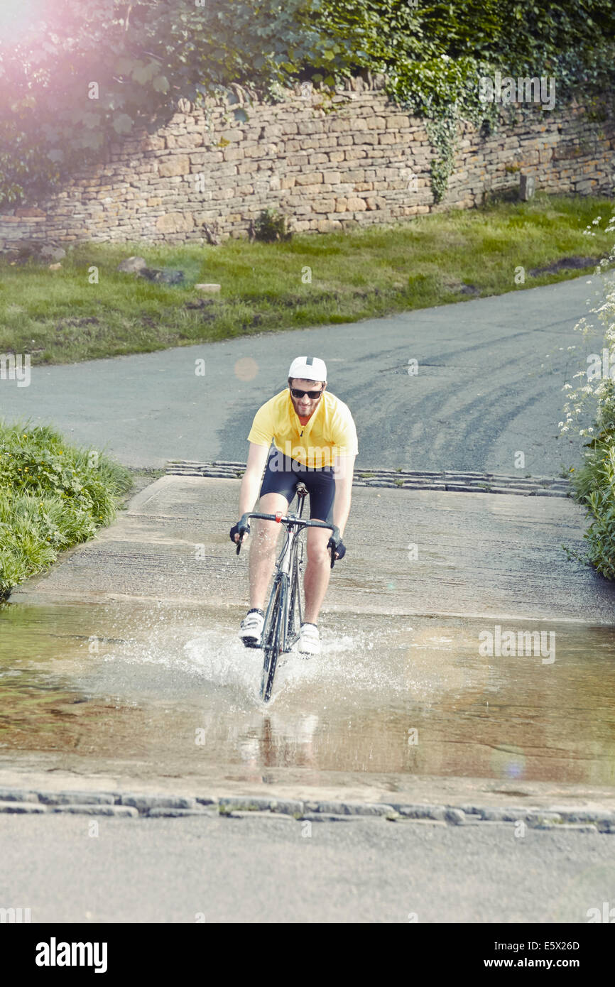 Ciclista a cavallo su strada allagata, Cotswolds, REGNO UNITO Foto Stock
