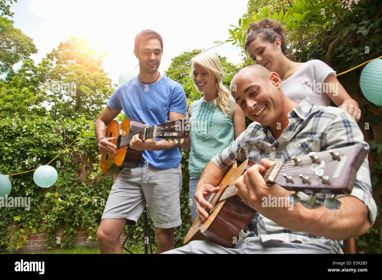 Maschio di amici a giocare la chitarra acustica in giardino per fidanzate Foto Stock