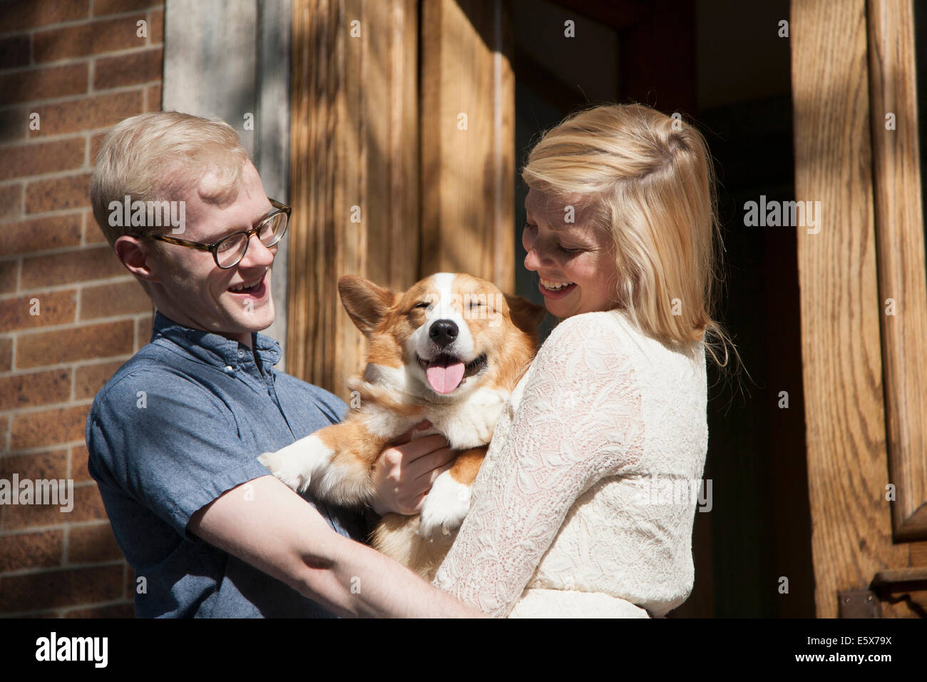 Felice coppia giovane con cane corgi in armi al di fuori della porta anteriore Foto Stock