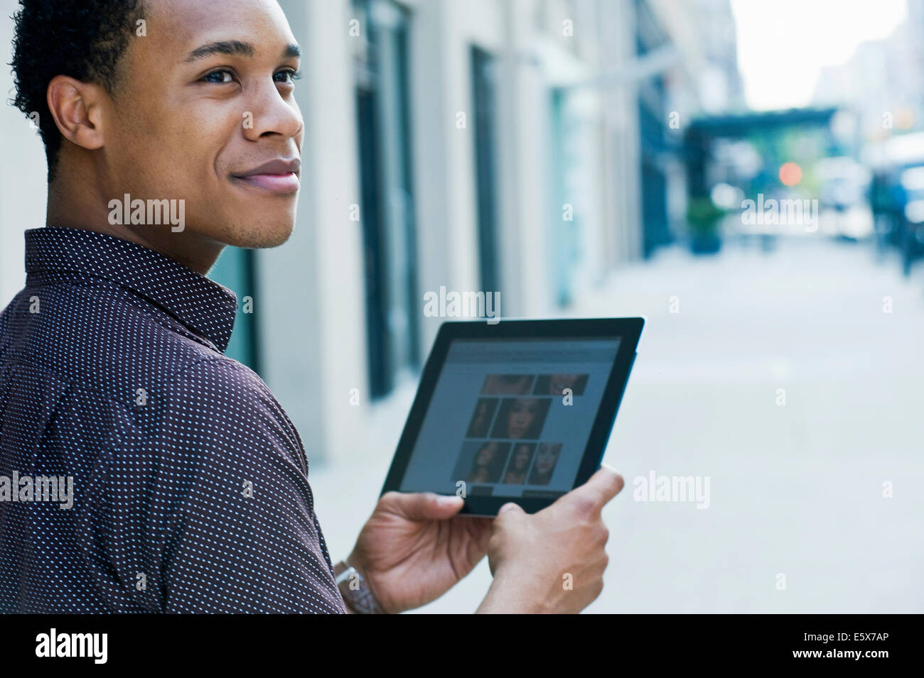 Giovane uomo sulla strada di città con tavoletta digitale e guardando sopra la spalla Foto Stock