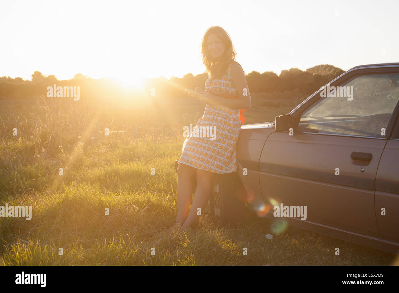 Ritratto di metà donna adulta appoggiata contro auto al tramonto Foto Stock