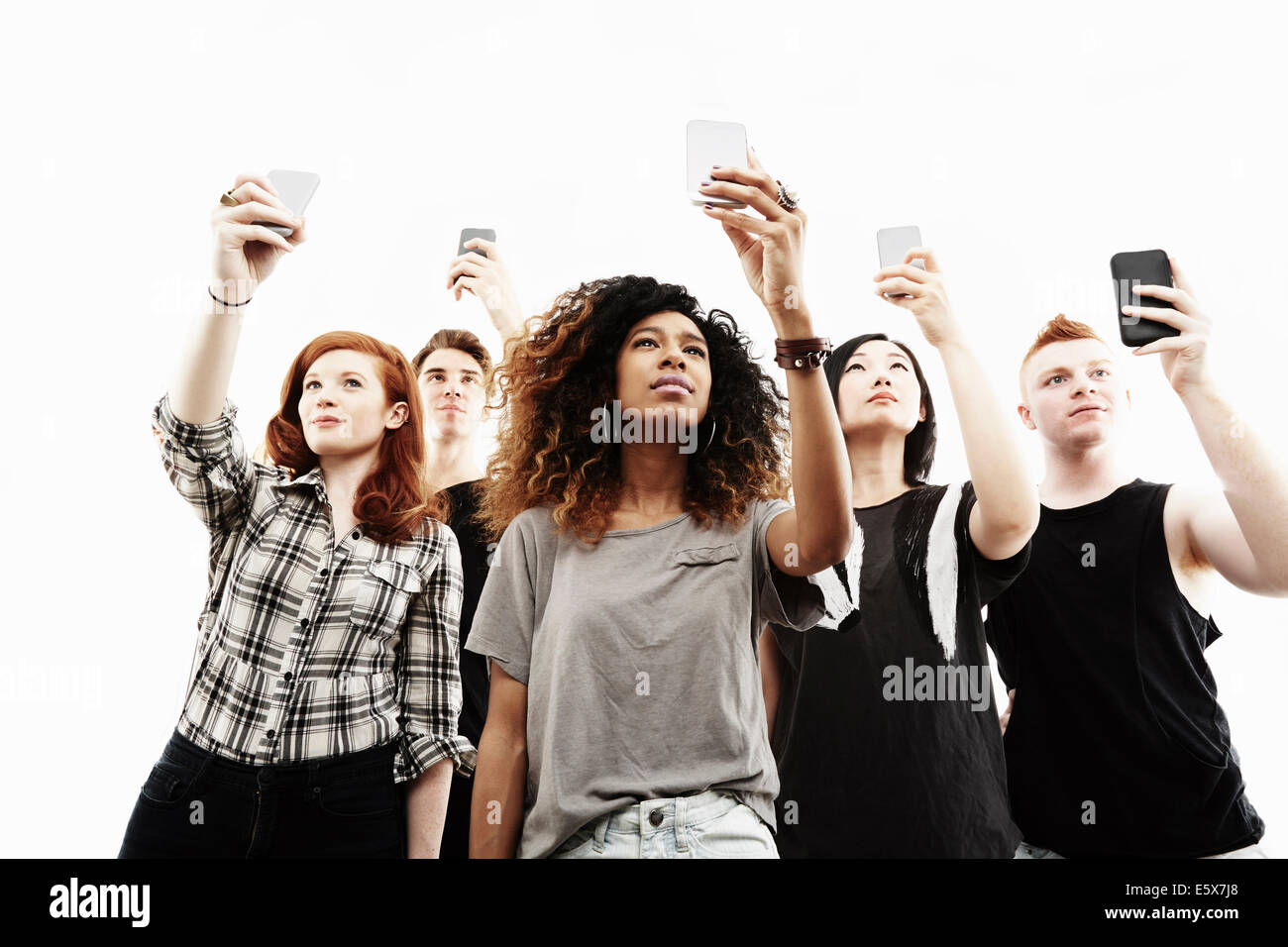 Ritratto in studio di cinque giovani adulti tenendo selfies sugli smartphone Foto Stock