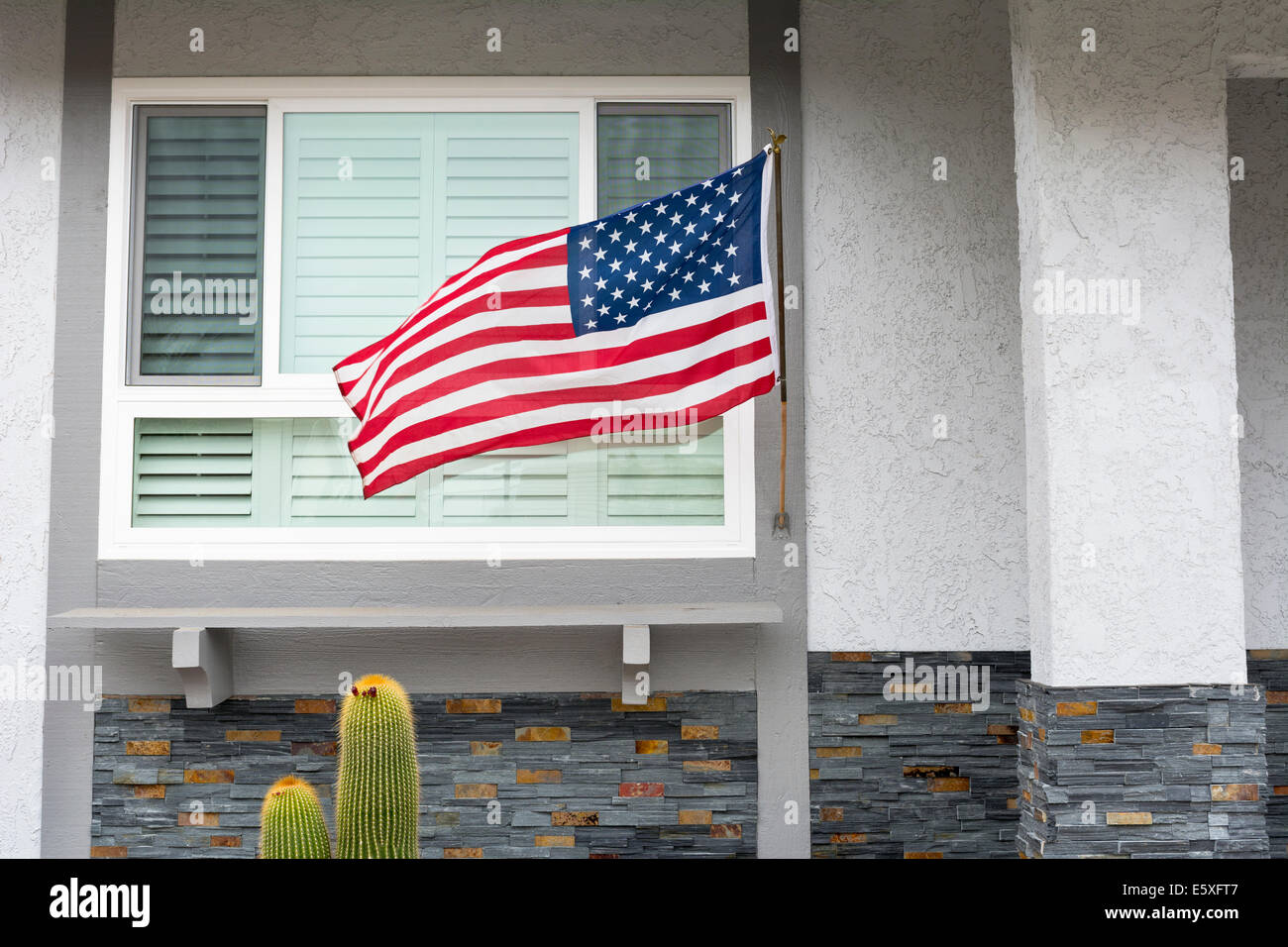 Bandiera americana che soffia nella brezza mentre è appesa su una casa residenziale simboleggia una vacanza patriottica negli Stati Uniti. Foto Stock