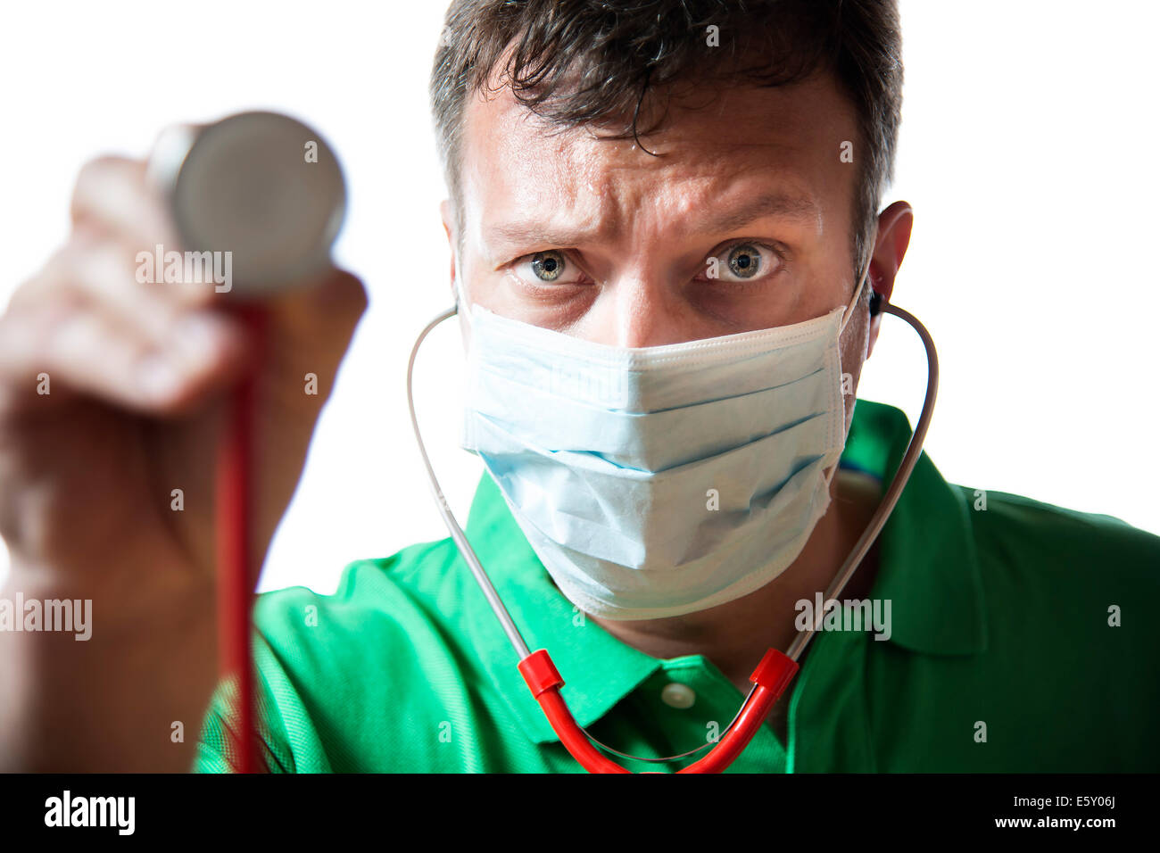 Desperate medico con mascherina chirurgica in camicia verde tenendo il suo stetoscopio Foto Stock