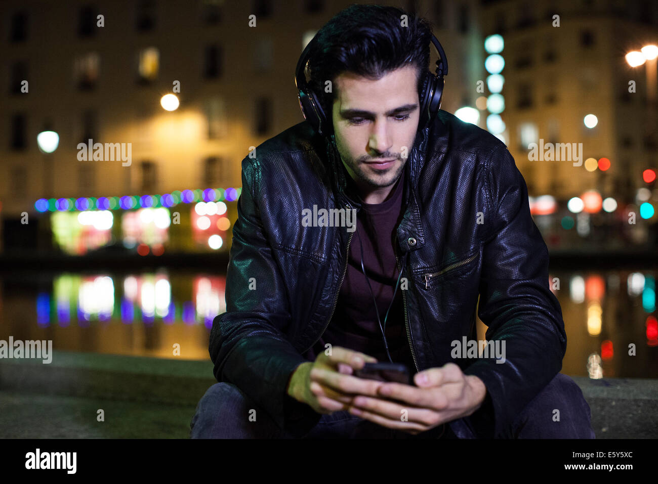 Giovane uomo seduto da solo all'aperto durante la notte per ascoltare  musica con le cuffie Foto stock - Alamy