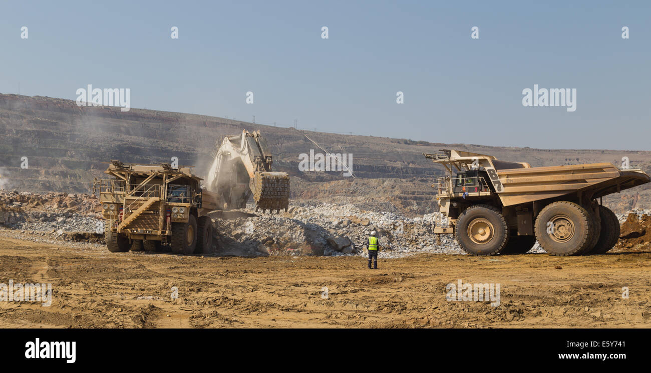 Un supervisore dirige Hitatchi haul carrelli essendo caricati con minerali da una massiccia escavatore Liebherr in un cielo aperto miniera di rame. Foto Stock