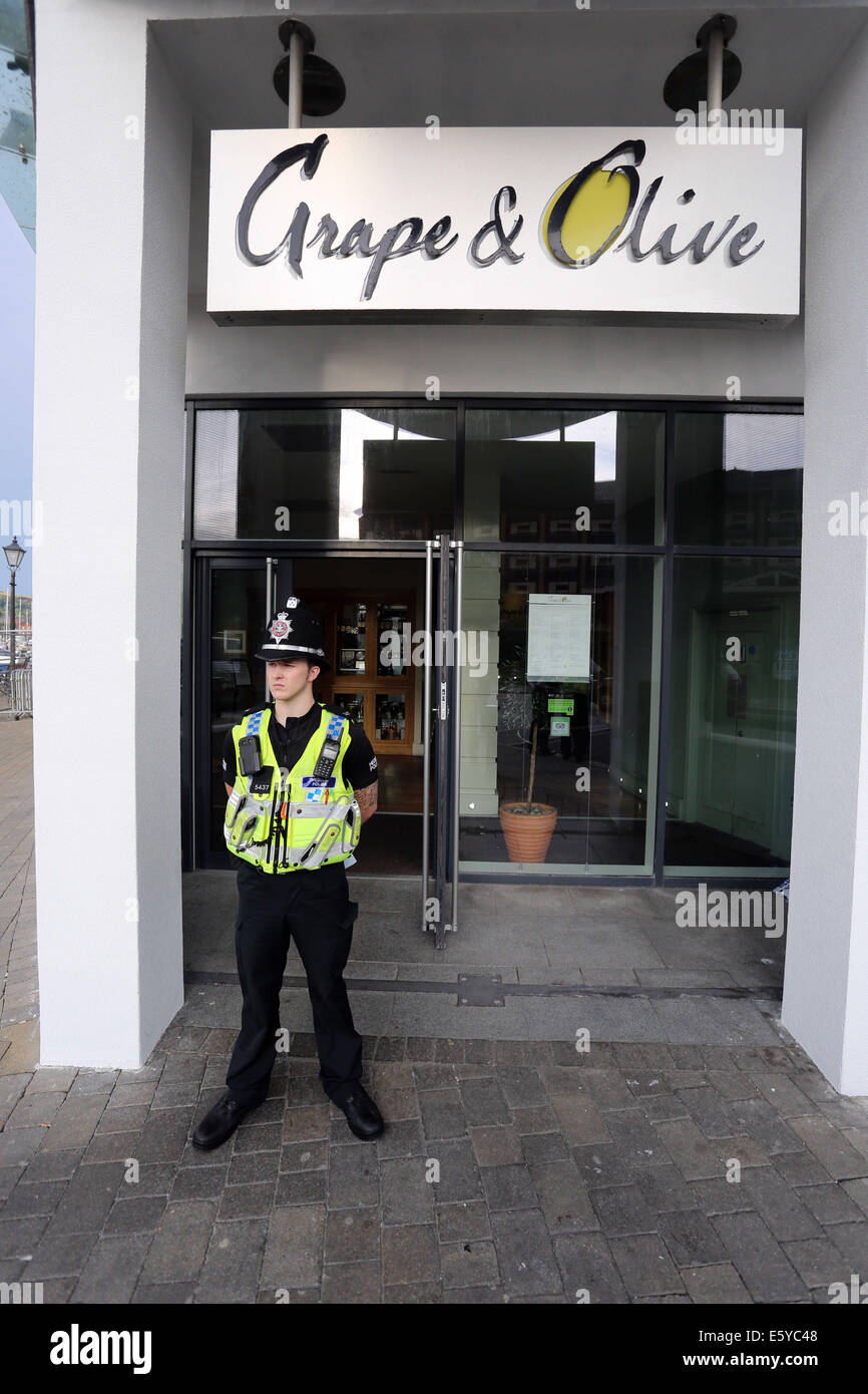 Swansea, Wales, Regno Unito. 8 agosto, 2014. Nella foto: l'attività di polizia all'ingresso delle uve e olive Restaurant nel meridiano Quay, Swansea, Galles del Sud. Venerdì 08 Agosto 2014 Re: Galles del Sud la polizia può confermare che una situazione con ostaggi del ventottesimo piano del meridiano Tower a Swansea Marina, ha concluso pacificamente con assenza di lesioni gravi. Gli ufficiali sono stati chiamati per la costruzione a 4pm venerdì 8 agosto dopo che un uomo è stato preso in ostaggio all'interno di un area pubblica dell'edificio, da un altro uomo che era in possesso di un'arma da fuoco. Credito: D Legakis/Alamy Live News Foto Stock