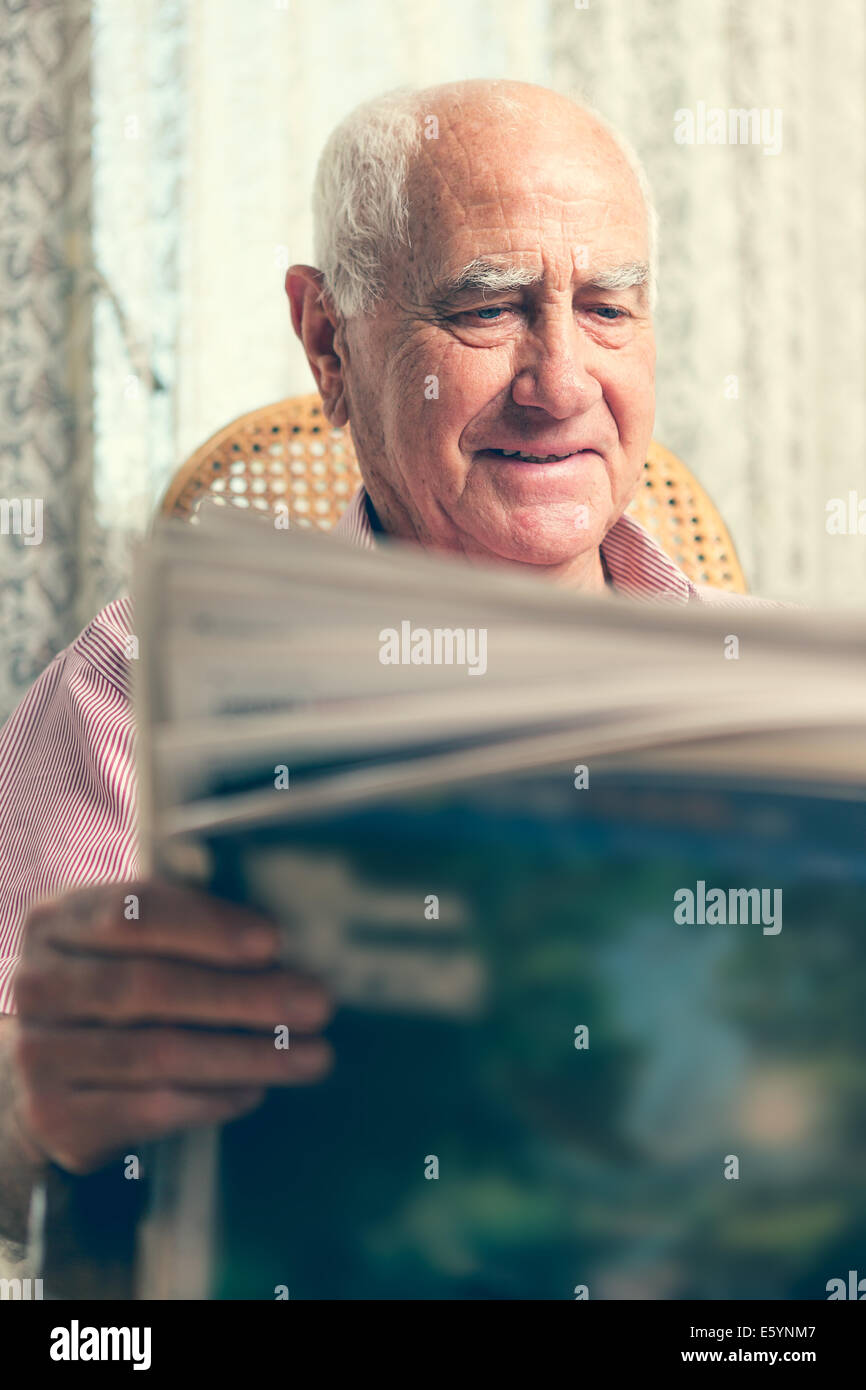 Uomo anziano seduto sulla sedia leggendo il giornale a casa Foto Stock