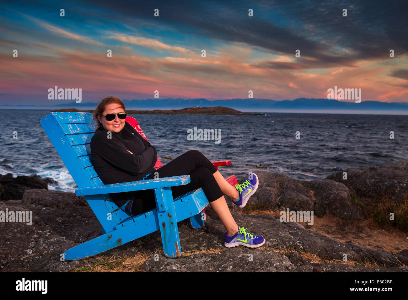 Ritratto di giovane donna seduta in blu Adirondack sedia-McNeil Bay, Victoria, British Columbia, Canada. Foto Stock