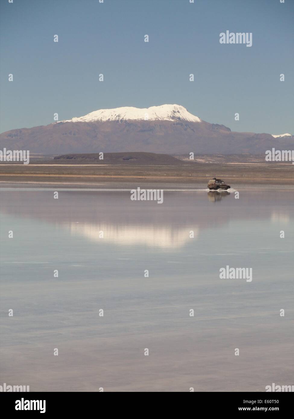 Un Land Cruiser attraversa la allagato Salar de Uyuni con il vulcano Tunupa nel contesto Foto Stock