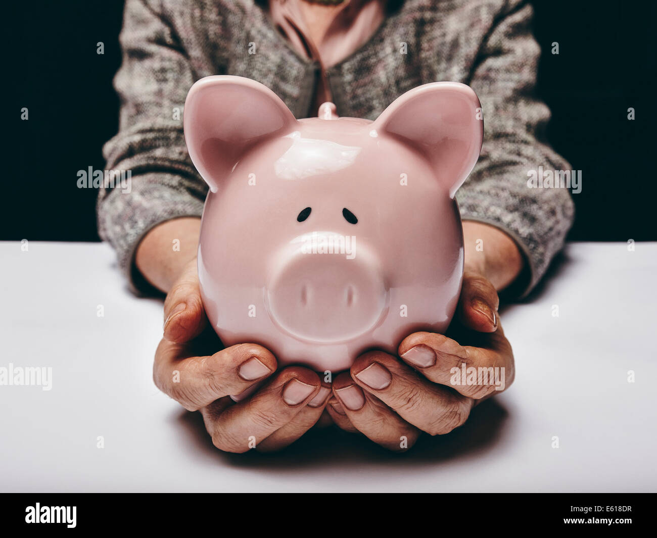 Close-up shot di donna anziana azienda rosa denaro pig-box. Senior donna mani piggybank. Concetto di risparmio di denaro. Foto Stock