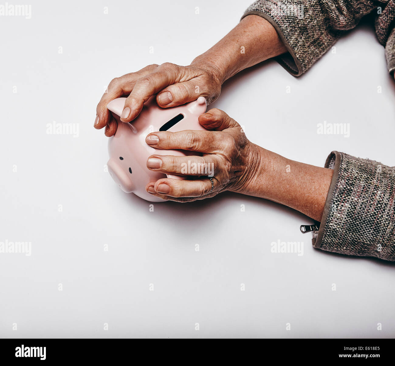 Vista superiore della donna senior mani tenendo un salvadanaio sulla superficie grigia. Anziani mani afferrando un salvadanaio. Il concetto di sicurezza Foto Stock