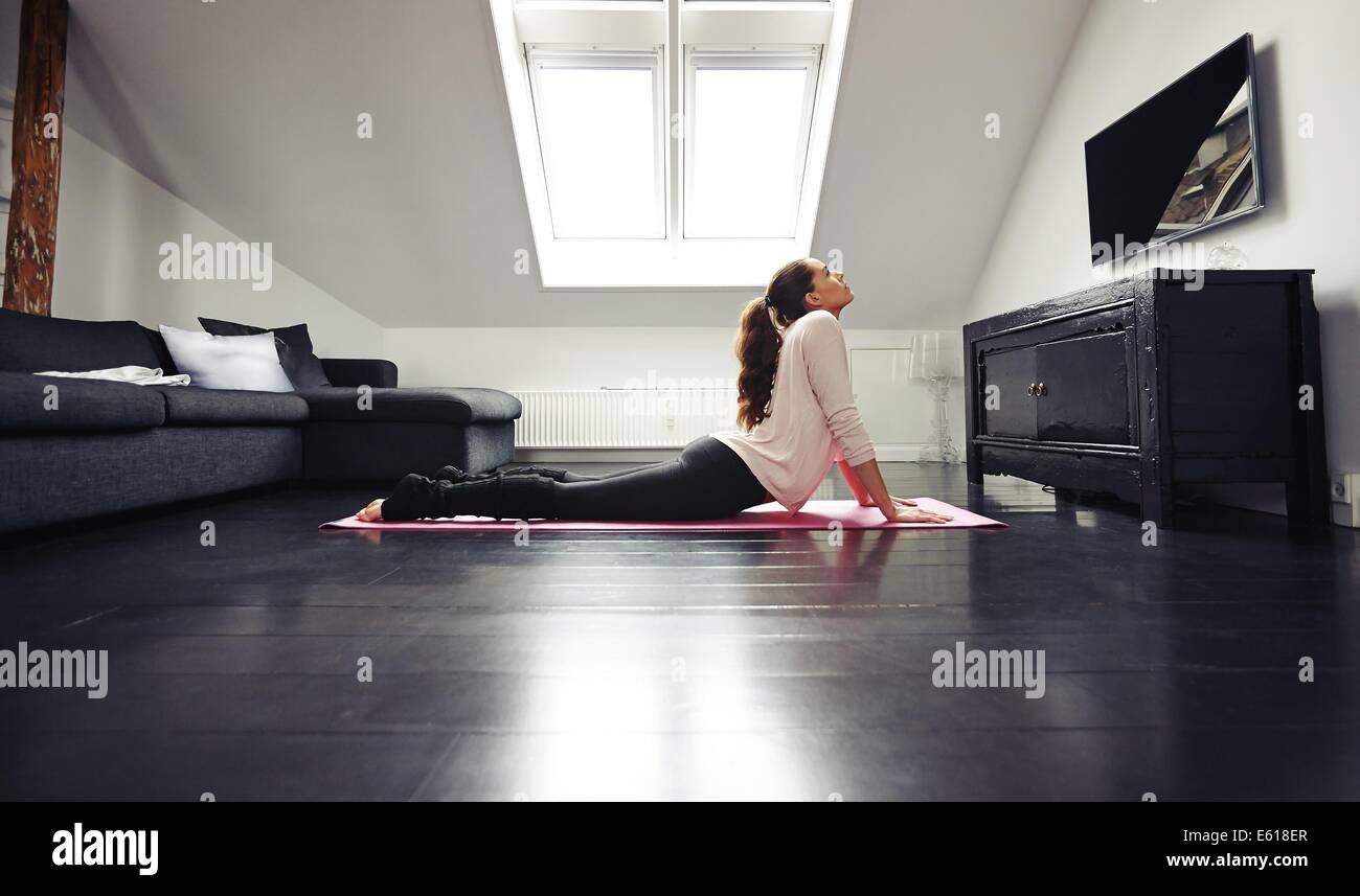 Bruna giovane donna che lavorano fuori esercizio di stiramento sul pavimento. Fitness modello femminile che esercitano sul tappetino a casa. Foto Stock