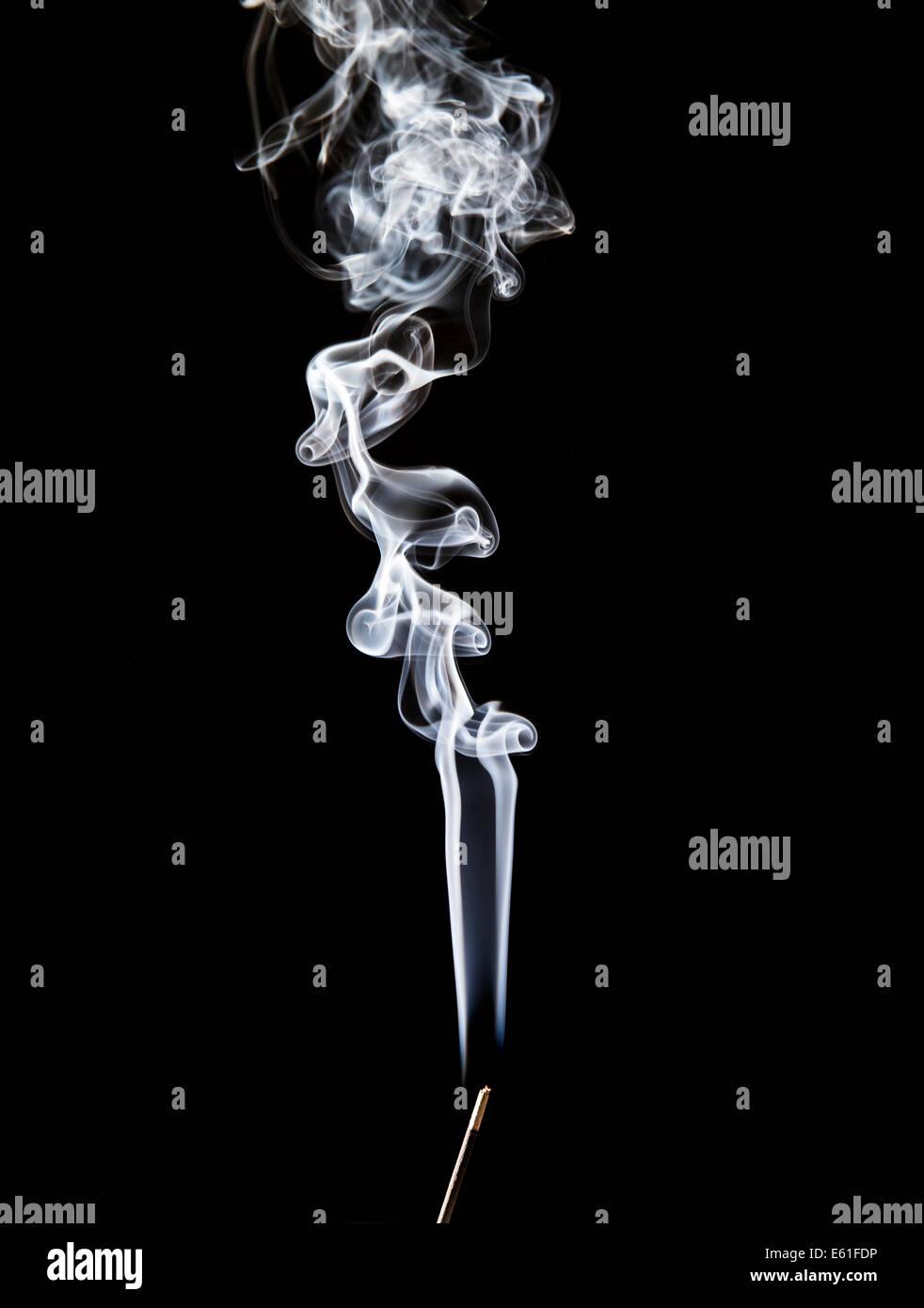 Filo di fumo derivante da un appena visibile joss stick contro uno sfondo nero Foto Stock