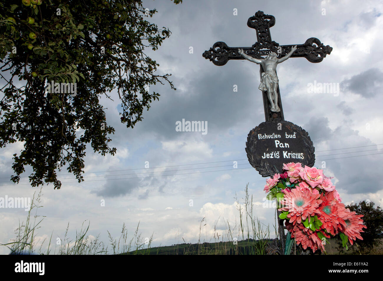 Edicola croce con Gesù e rosso fiori di plastica nel paese Foto Stock