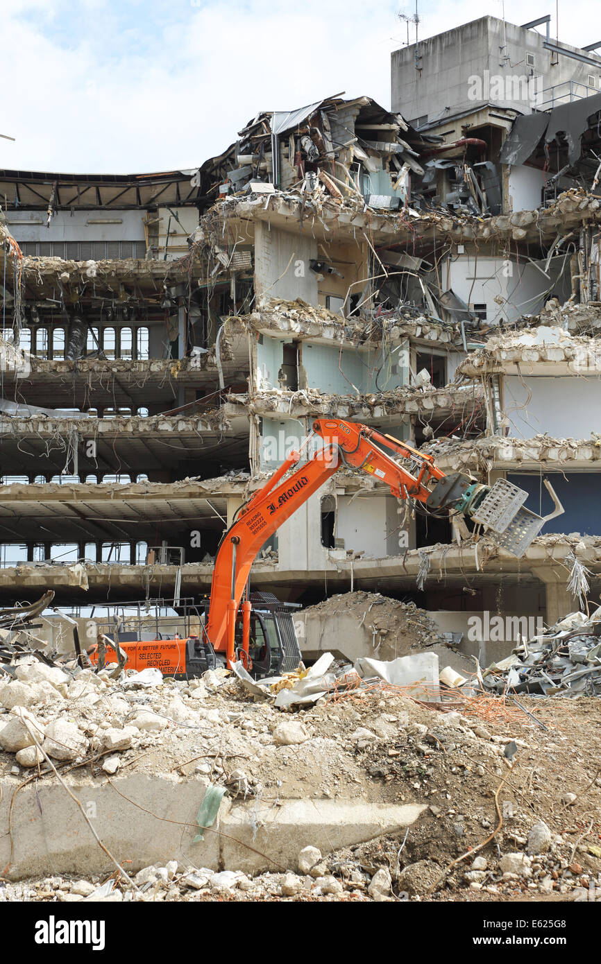 Un edificio a sei piani in cemento armato edificio ufficio in lettura è demolita utilizzando idraulico, escavatori cingolati Foto Stock