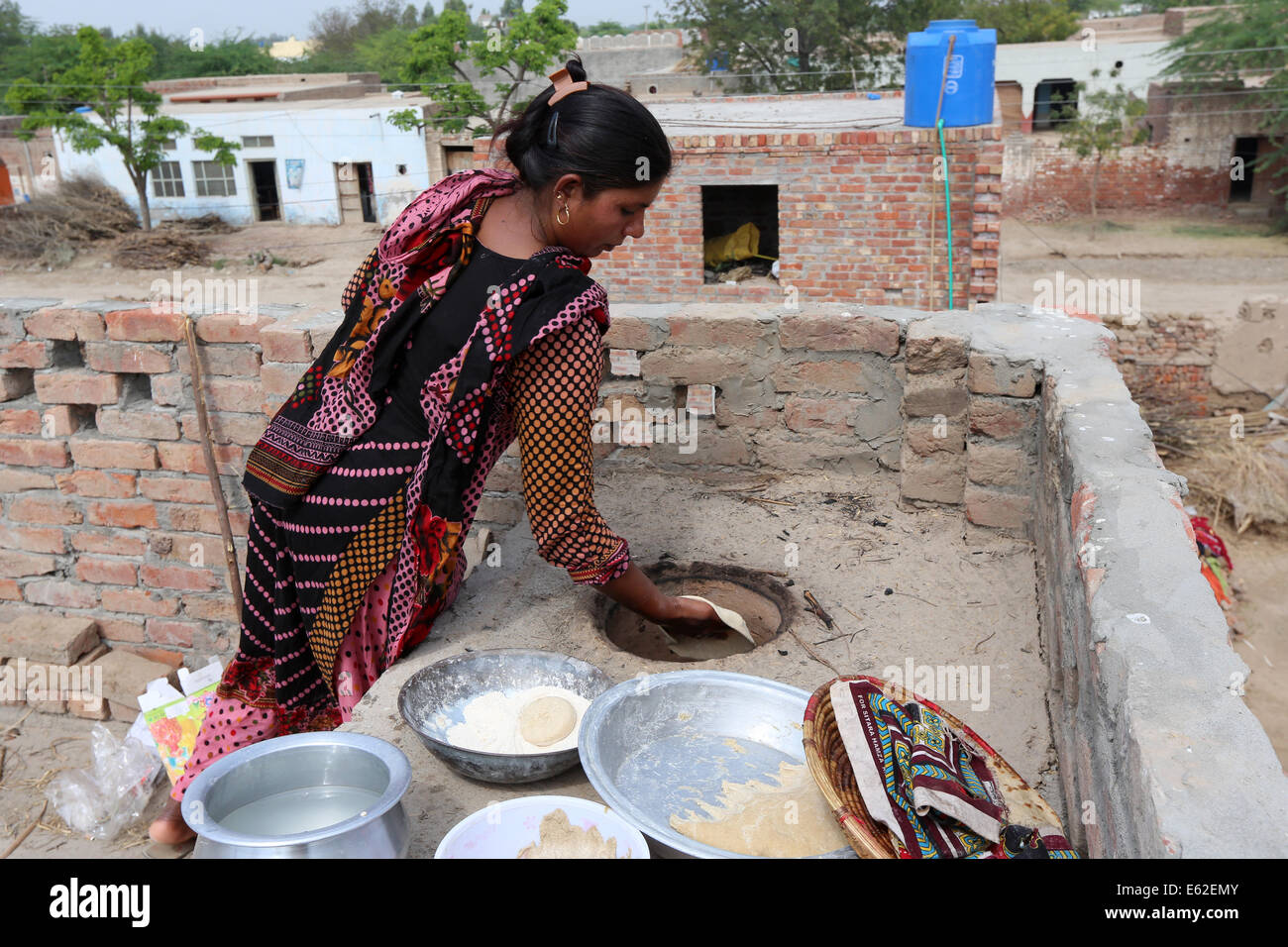 Donna in abito tradizionale cottura roti pane (noto come chapati) in un forno di argilla. Villaggio di Khushpur, Provincia del Punjab, Pakistan Foto Stock