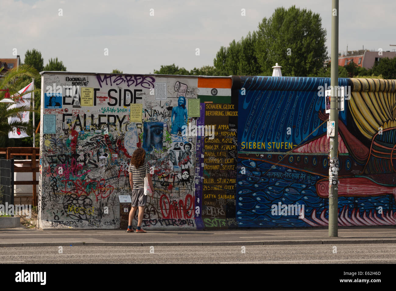 Una fotografia di un uomo in piedi di fronte alla East Side Gallery di Berlino. La East Side Gallery è un memoriale internazionale. Foto Stock
