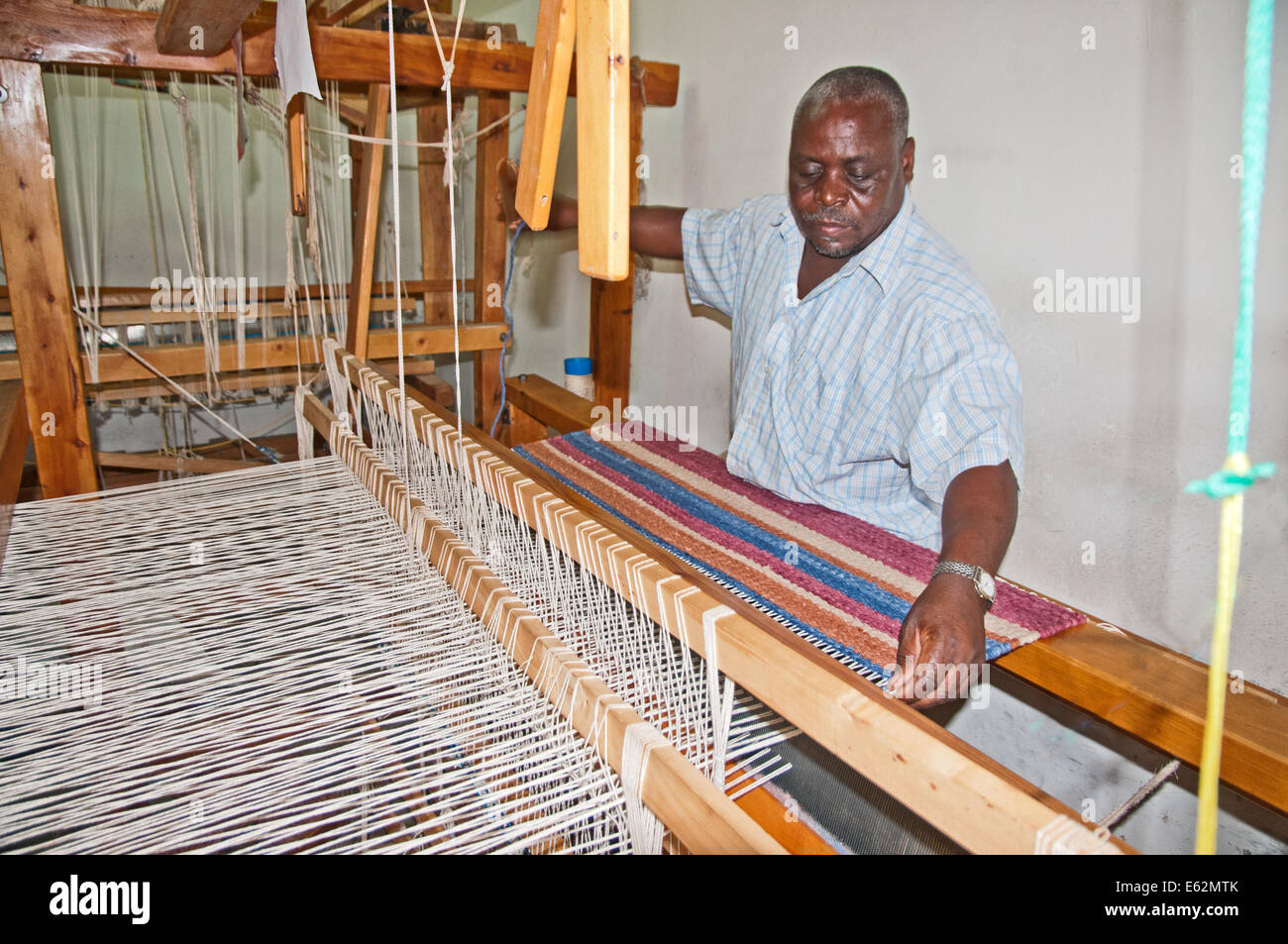 Nero uomo africano tessitura di un tappeto di lana sul telaio in corrispondenza di tessitori Elmentieta sulla strada del lago Naivasha Kenya Africa telaio tessitore di armatura RUG Foto Stock