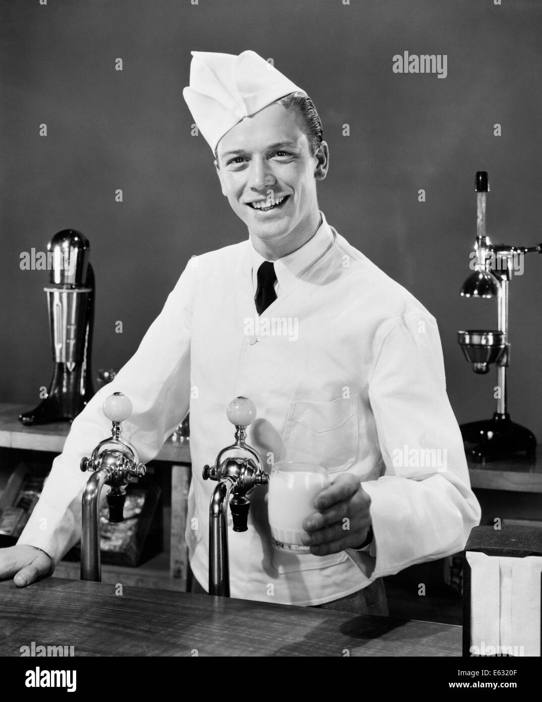 Negli anni quaranta anni cinquanta sorridente SODA JERK DIETRO IL CONTATORE tenendo un bicchiere di latte Foto Stock