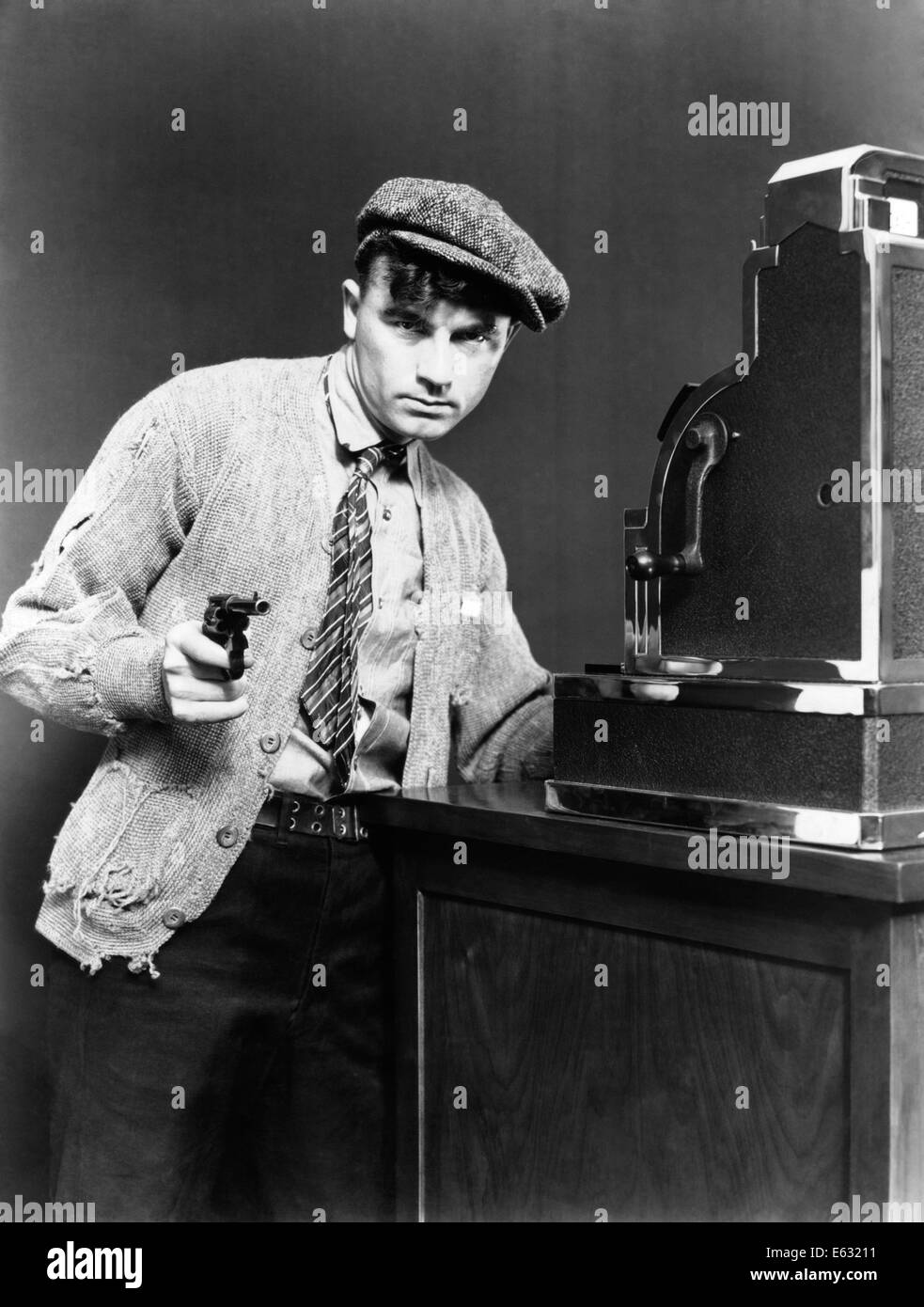 1930s uomo disperato rapinatore pistola di puntamento prendendo denaro dal registratore di cassa indossando indumenti strappati depressione ERA LA CRIMINALITÀ Foto Stock