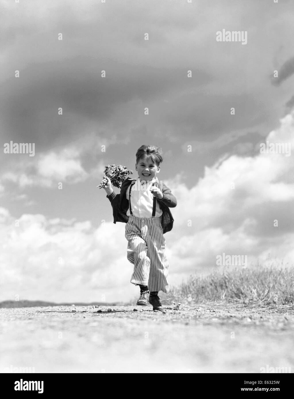 Negli anni quaranta anni cinquanta BOY IN ESECUZIONE VERSO LA TELECAMERA SUL PAESE LA TENUTA DI STRADA bouquet di fiori di primavera in una mano Foto Stock