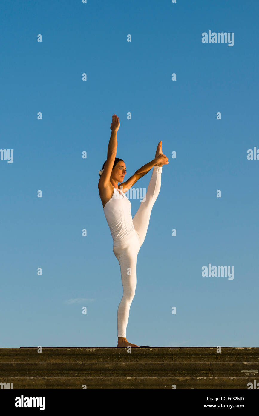 Giovane donna pratica di Hatha yoga, all'aperto, che mostra la posa Anjaneyasana, mano sollevata alla posa del piede Foto Stock