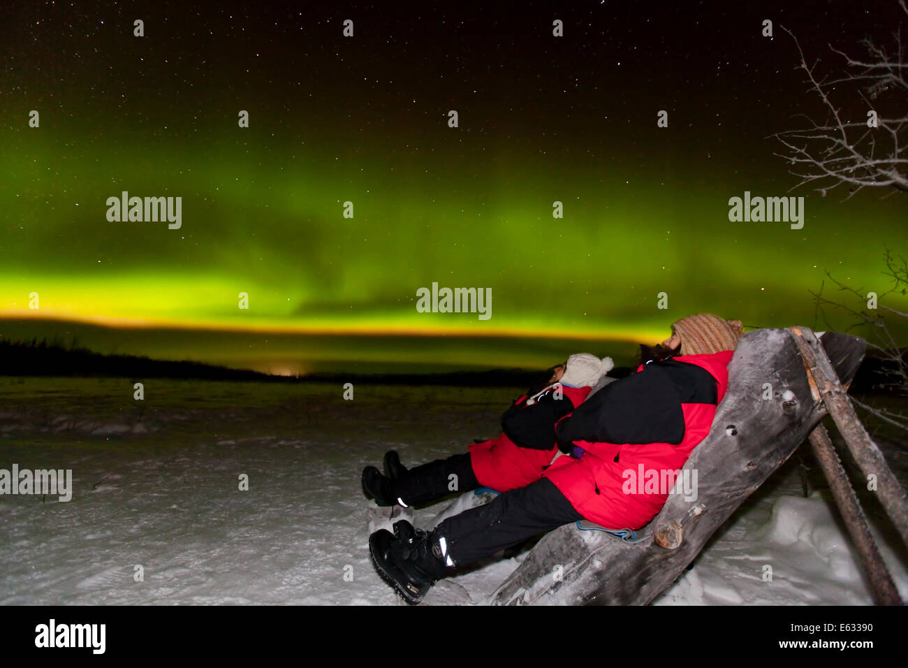 Due persone sedute in una sedia in legno, guardando polare settentrionale luci, vicino a Whitehorse, Yukon Territory, Canada Foto Stock