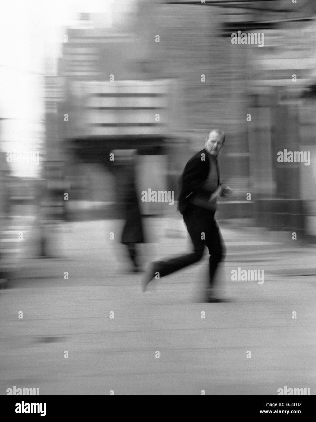 Anni Settanta motion blur uomo che corre lungo una strada di città guardando sopra la sua spalla la paura della criminalità Foto Stock