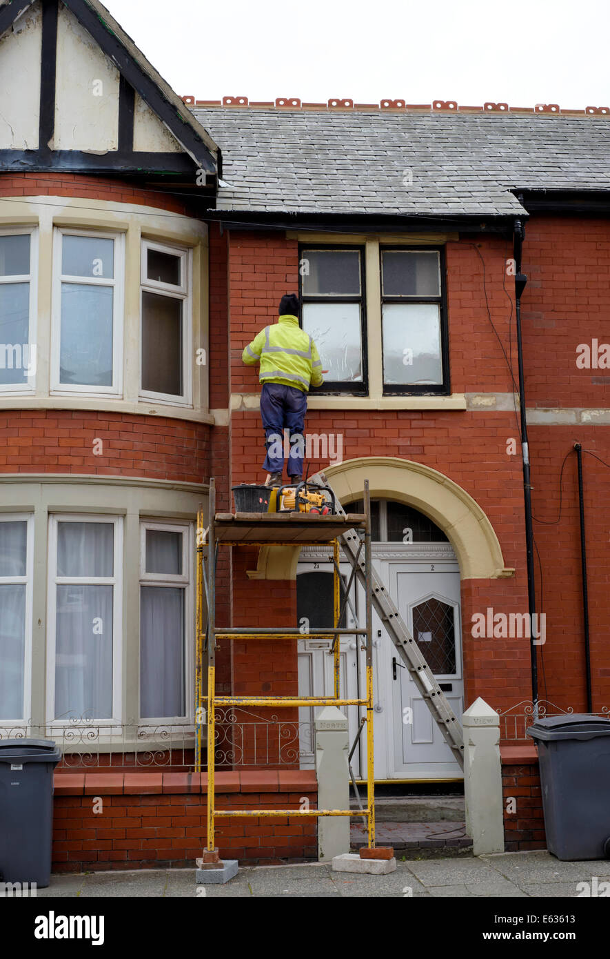 Uomo sulla torre di impalcatura repointing cotto sulla parte anteriore di una casa a schiera Foto Stock