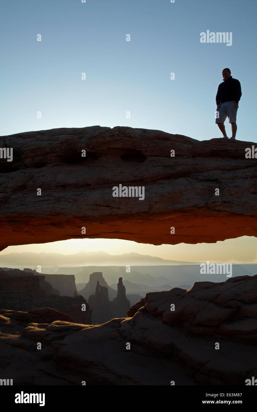 Persona sulla Mesa Arch e sunrise oltre La Sal Mountains, il Parco Nazionale di Canyonlands, Utah, Stati Uniti d'America Foto Stock
