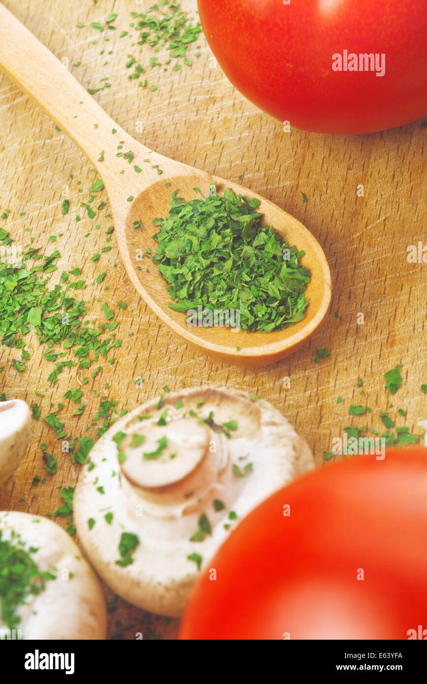 Prezzemolo tritato sul cucchiaio di legno in cucina. Preparazione alimentare dello sfondo. Foto Stock