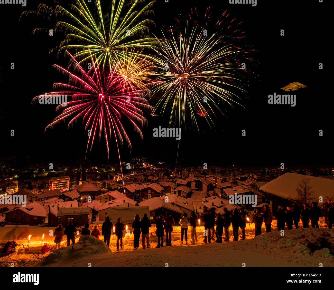 Il nuovo anno ha festeggiato in Saas-Fee, alpi svizzere, con un display di grandi dimensioni di fuochi d'artificio. Le persone con le torce cercano di massa elevata per guardare. Foto Stock