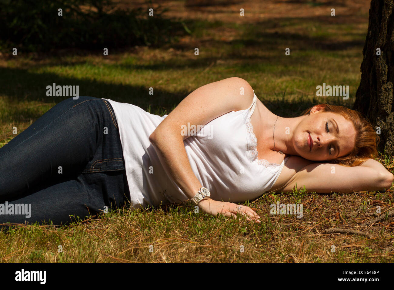 Un bel giovane dai capelli rossi ragazza dorme nel parco. Addormentato sotto un albero e giacente sull'erba nel caldo sole. Foto Stock