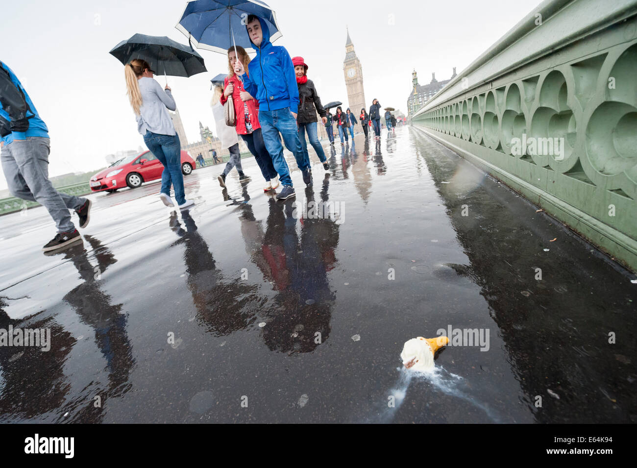 Westminster Bridge, Londra, Regno Unito. Il 14 agosto 2014. Acquazzoni pesanti ha colpito Londra oggi come il Met Office emessi avvisi di maltempo e l'Agenzia dell'ambiente ha messo 19 avvisi alluvione in tutto il paese di cui 8 nel sud-est. Nella foto: Un abbandonato il gelato è lasciato sul marciapiede di Westminster Bridge come turisti passano sotto la pioggia. Credito: Lee Thomas/Alamy Live News Foto Stock