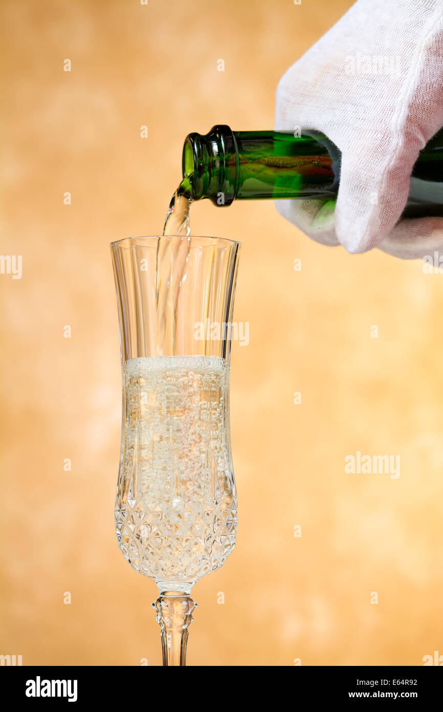 Un cameriere versa, croccante, delizioso champagne in un elegante vetro, pronti contro una golden, sfondo a chiazze. Foto Stock