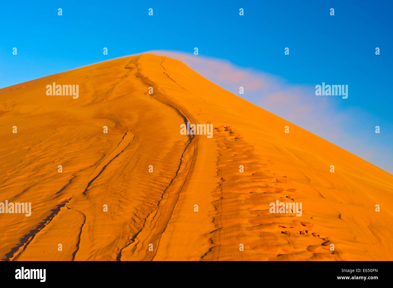 Il vento soffia sabbia fine sulla cresta di una Duna Erg Chebbi, la sabbia del deserto del Sahara,, nel sud del Marocco, Marocco Foto Stock