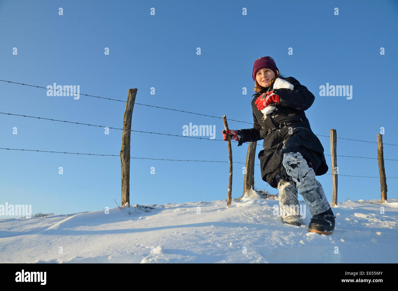 Ragazza camminare da una recinzione di contenimento palle di neve su un inverno nevoso giorno Foto Stock